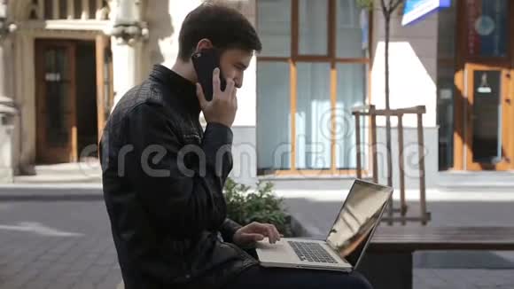 年轻人在街凳上用手提电脑用智能手机说话视频的预览图