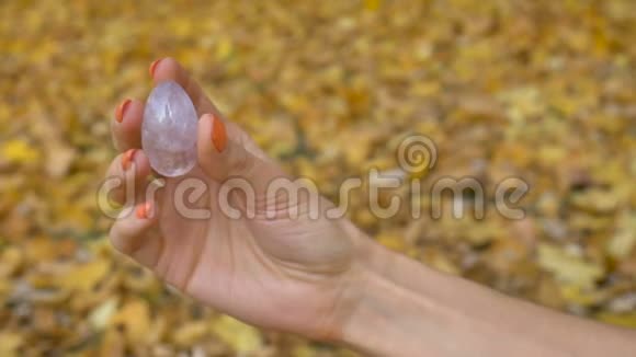 带橙色指甲的女性手拿着透明紫罗兰紫水晶玉尼蛋用于Vumfit冥想视频的预览图