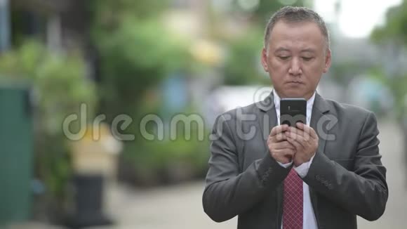成熟的日本商人在户外大街上用电话视频的预览图
