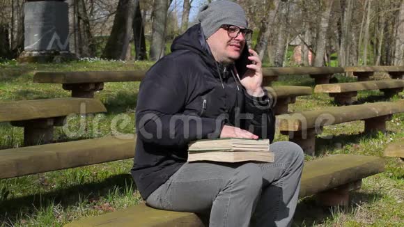 有两本书和智能手机的人坐在公园的长椅上视频的预览图