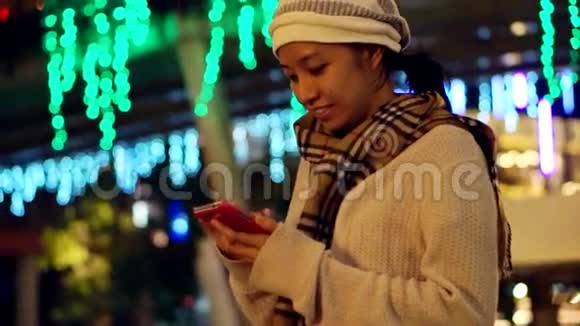以圣诞灯为背景的亚洲女孩在节日期间使用智能手机的视频通信摘要视频的预览图