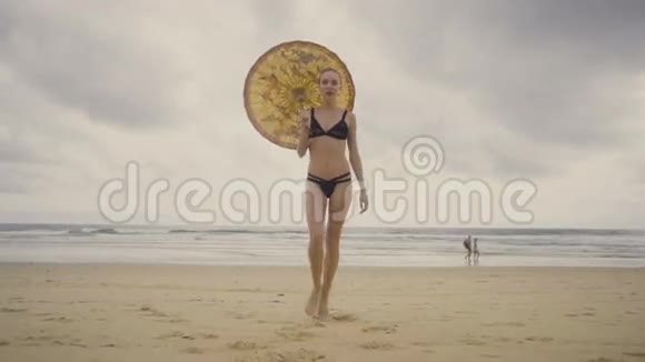性感迷人的女人穿着黑色比基尼在海滩上打着中国伞视频的预览图