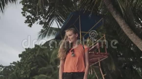 年轻的金发女人独自站在海滩上看日落视频的预览图