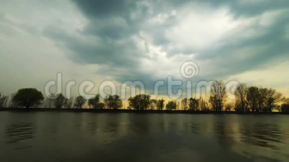 宁静的野蛮景象一阵轻风吹过水面狂风暴雨般的云朵掠过河岸上的树木日落时分视频的预览图