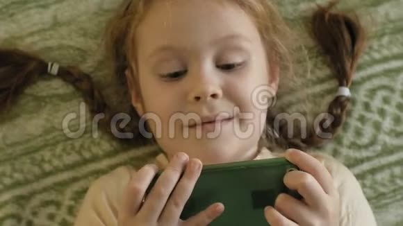 幸福的女孩金发和辫子躺在沙发上用电话微笑肖像视频的预览图