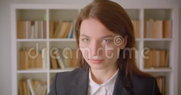 一位年轻的白种人女商人在室内图书馆里看着镜头微笑的特写画像视频的预览图
