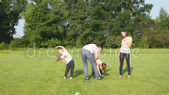 漂亮的家庭在户外做体育运动家庭在草地上的足球场上倾斜和做运动视频的预览图