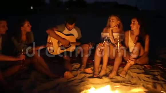 日落海滩派对篝火晚会朋友们围坐在篝火旁喝着啤酒对着吉他唱歌青年视频的预览图