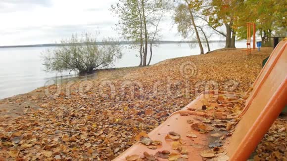 秋天的公园树叶落在大湖的长凳上黄色的树叶在沙滩上缓慢地翻滚视频的预览图