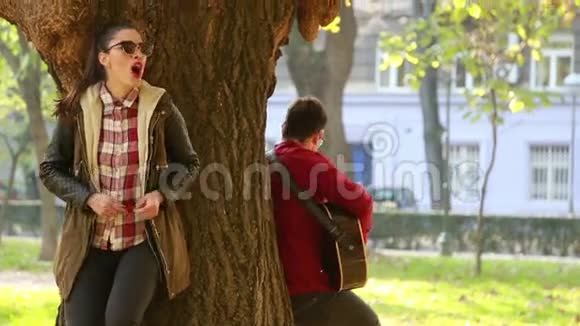 女人唱歌男人弹吉他靠在公园的树上视频的预览图