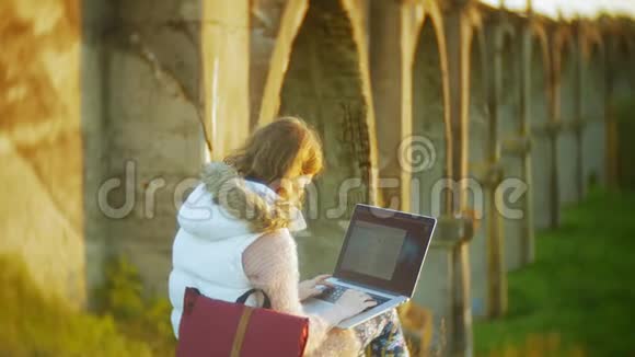 年轻女子在老式铁路桥附近的笔记本电脑上工作视频的预览图