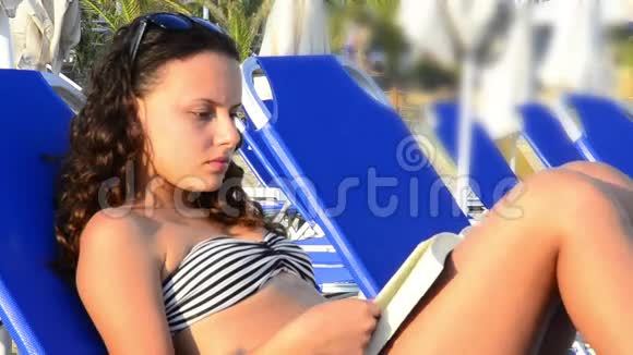 快乐美丽的少女日光浴和阅读书在海滩高清视频的预览图