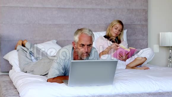 男人躺在床上手里拿着笔记本电脑挨着妻子视频的预览图
