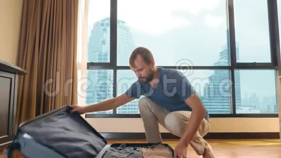 一个英俊的男人把一个手提箱装在一个房间里里面有一扇俯瞰摩天大楼的全景窗视频的预览图