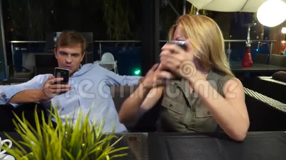 一对情侣在户外咖啡馆谈恋爱男人和美女约会所有人都在看他的手机4K视频的预览图