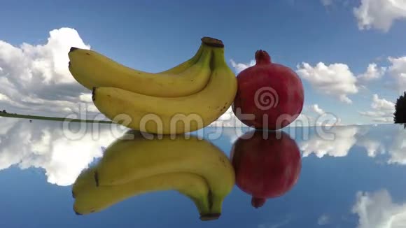 三个香蕉和一个石榴放在镜子玻璃上时间流逝4K视频的预览图