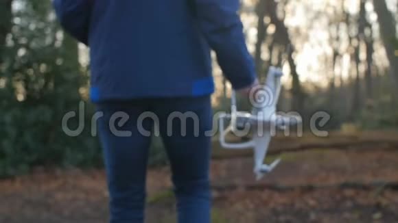 一个穿着蓝色夹克的人带着一架无人机缓慢地穿过森林视频的预览图