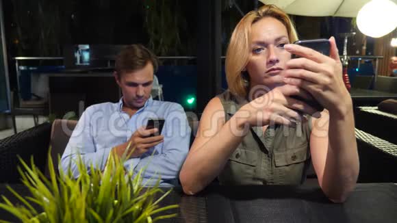 一对情侣在户外咖啡馆谈恋爱男人和美女约会所有人都在看他的手机4K视频的预览图