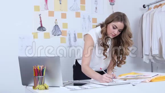 时装设计师为新的收藏品绘制草图然后看电脑视频的预览图