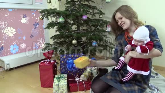 快乐的女人在圣诞树旁展示她可爱的婴儿礼盒视频的预览图
