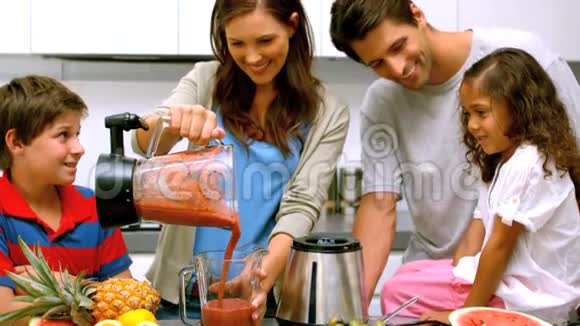 带着家人从搅拌机里倒水果鸡尾酒的微笑女人视频的预览图