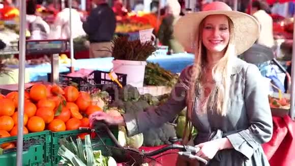 金发女孩骑着自行车站在市场上微笑着视频的预览图