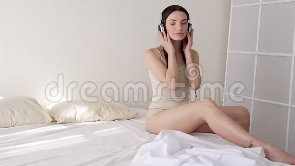 女孩坐在卧室的床上用耳机听音乐视频的预览图