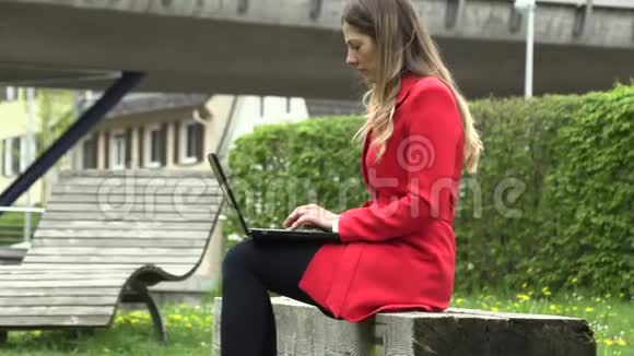 穿红裙子的女孩拿着笔记本电脑在街上工作视频的预览图