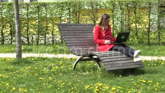 那个穿红裙子的女孩在公园的电脑上工作视频的预览图