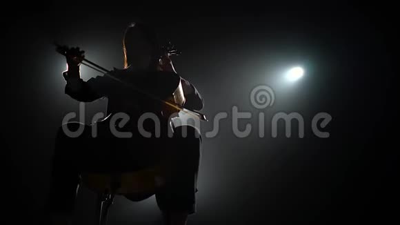 一个音乐家的剪影在一个黑暗的画室里有一个大提琴有灯笼黑烟背景视频的预览图