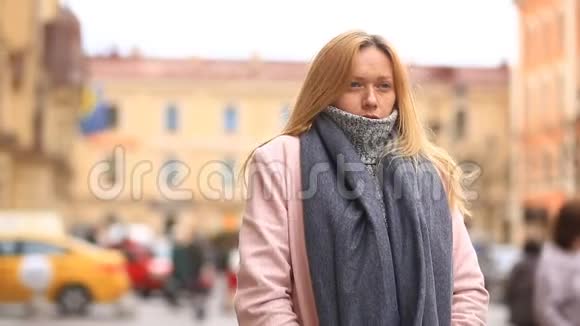 一个穿着粉红色外套和毛衣的疲惫的女人站在拥挤的街道中间从寒冷中退缩出来视频的预览图