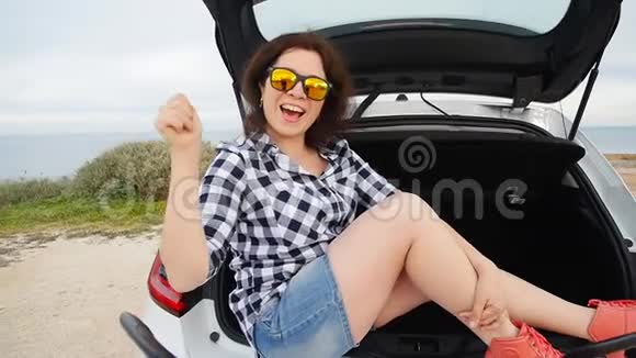 快乐的年轻女子暑假坐在汽车后备箱里视频的预览图
