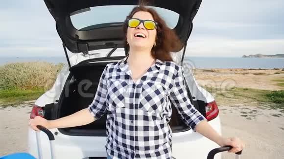 快乐的年轻女子暑假坐在汽车后备箱里视频的预览图