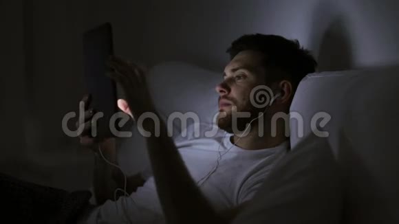 晚上床上有平板电脑和耳机的男人视频的预览图