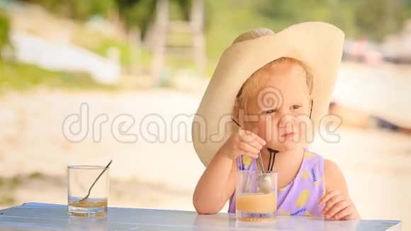 大帽子里的小金发女孩用勺子喝果汁视频的预览图