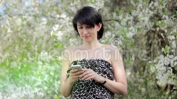 公园里有智能手机的年轻女人春天在一棵开花的树的背景下视频的预览图
