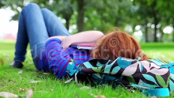 漂亮的年轻学生躺在书包上的草地上视频的预览图