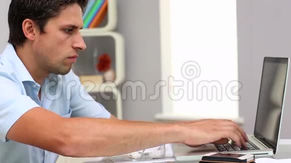 专注的有魅力男人在客厅里拿着笔记本视频的预览图
