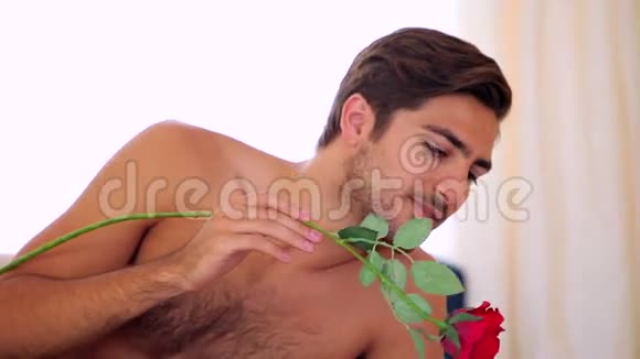 男人用一朵红玫瑰在床上挠他漂亮的女朋友视频的预览图