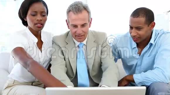 售货员在沙发上和顾客交谈向他们展示笔记本电脑视频的预览图