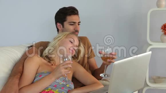 一对躺在沙发上看着手提电脑喝酒视频的预览图