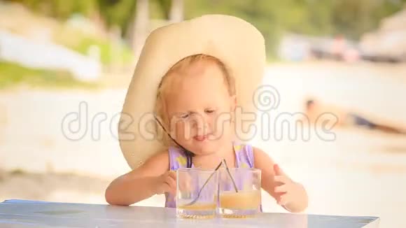戴帽子的小女孩用杯子里的勺子喝果汁视频的预览图