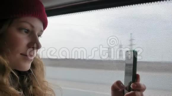 年轻开朗的女人戴着红帽子在一个悲伤的日子乘公共汽车旅行她在智能手机上拍照视频的预览图