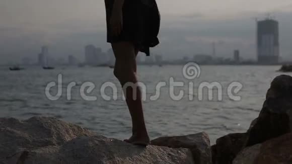 年轻女子站在沙滩上的石头上看着大海视频的预览图