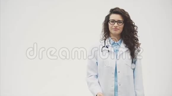 年轻漂亮的女医生穿着医用礼服在这段时间里她的背景是灰色的手里拿着一个白色的视频的预览图