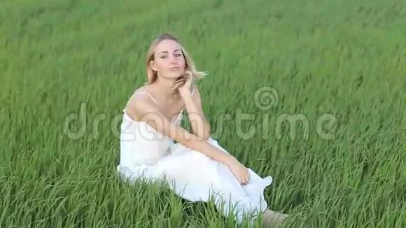 一个可爱的年轻女人坐在草地上在开阔的田野上看着摄像机视频的预览图