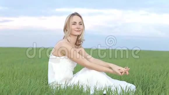 一个可爱的年轻女人坐在草地上在开阔的田野上看着摄像机视频的预览图