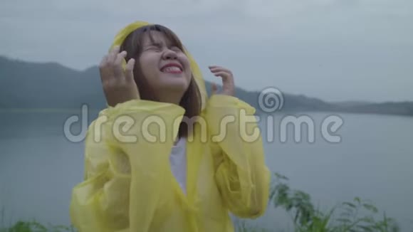 慢动作年轻的亚洲女人在湖边穿着雨衣玩雨时感到快乐视频的预览图