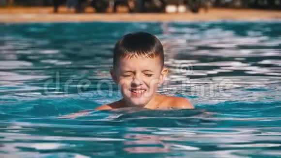 快乐的男孩在一个有蓝色水的游泳池游泳慢动作视频的预览图