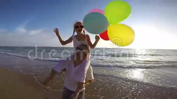在日落时分爸爸和女儿带着气球在海滩上玩耍视频的预览图